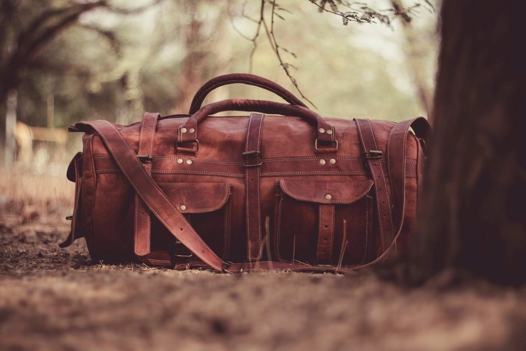 Brown leather duffel bag on a forest floor