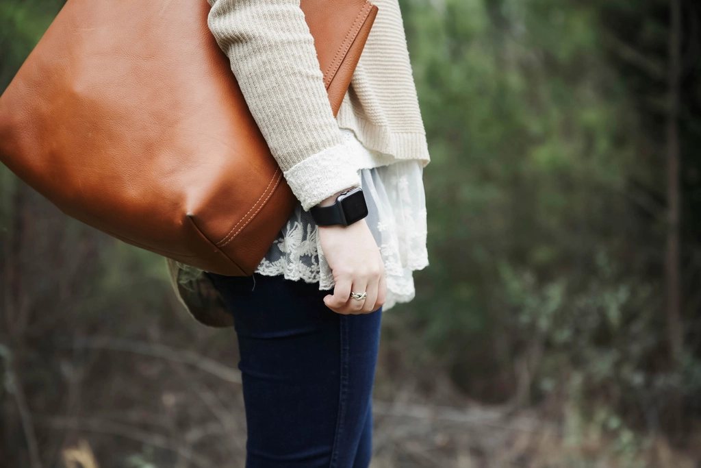 Cognac leather tote carried on the shoulder over a cream knit and lace top