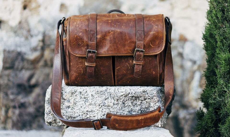 Distressed brown leather messenger bag resting on a granite block