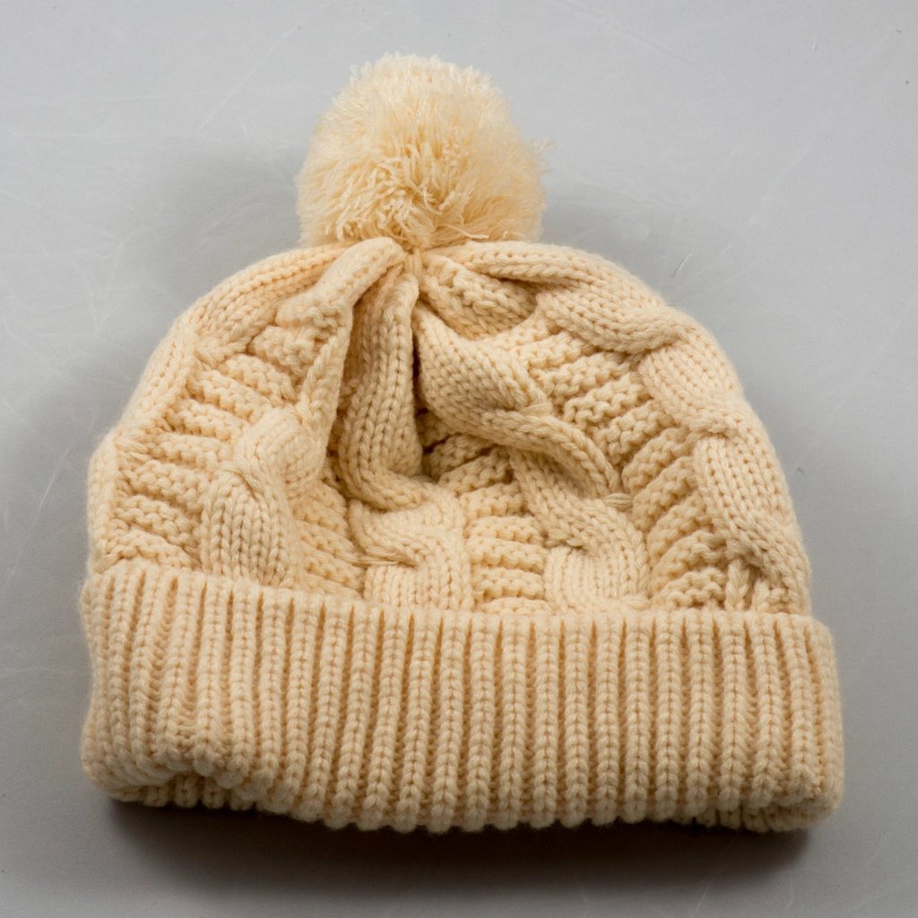 Cream cable-knit beanie with a pom-pom on a grey surface
