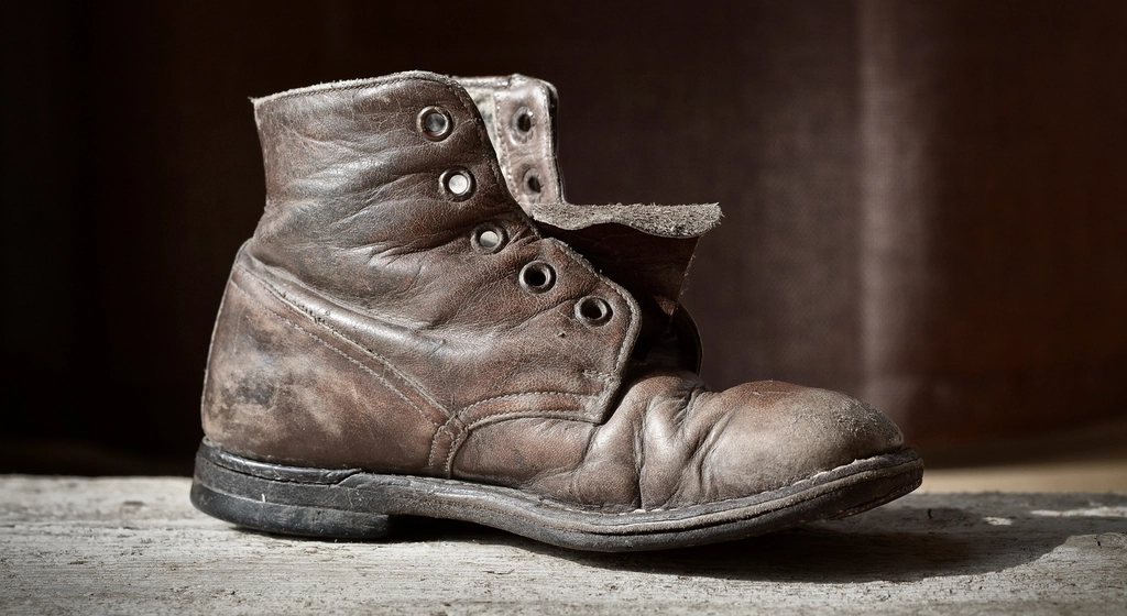 Single well-worn brown leather lace-up boot on a wooden plank