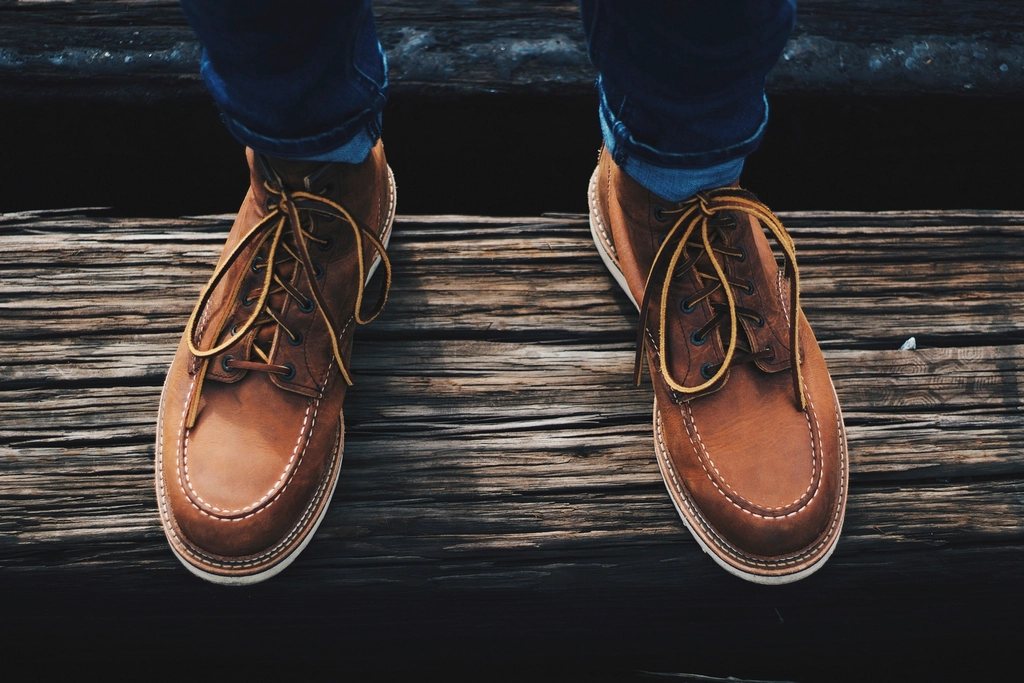 Tan leather moc-toe boots with cuffed jeans, seen from above on weathered wood
