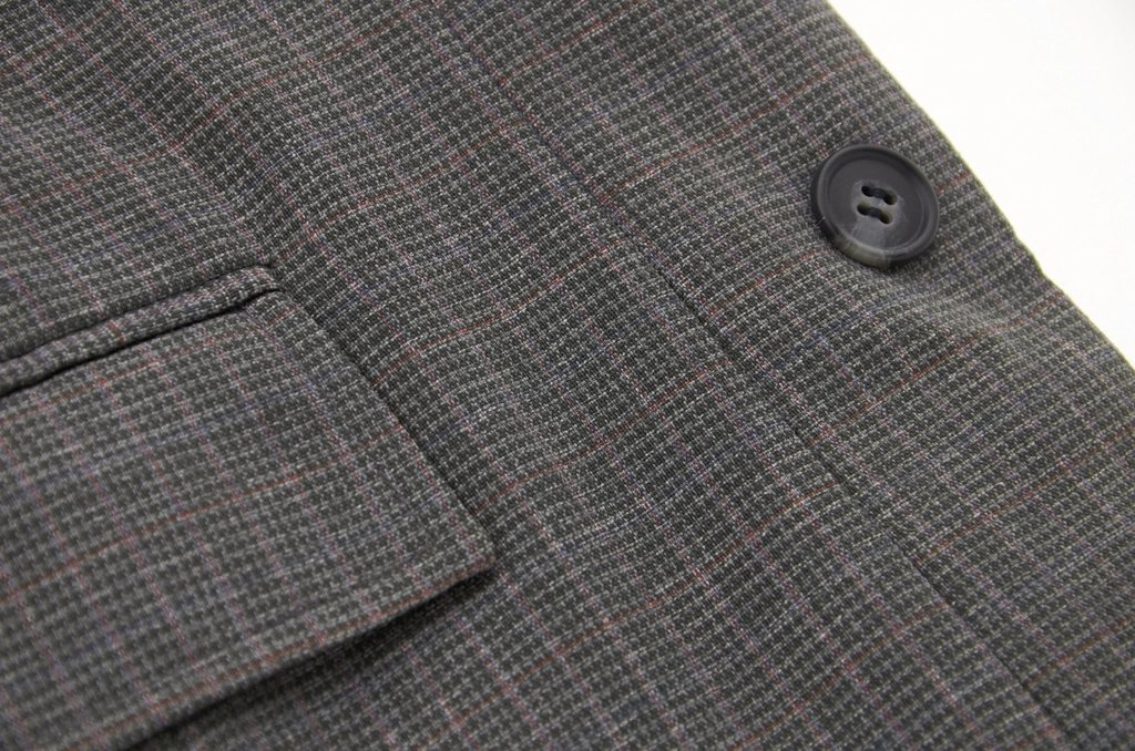 Close-up of a grey check wool coat with a pocket flap and horn button