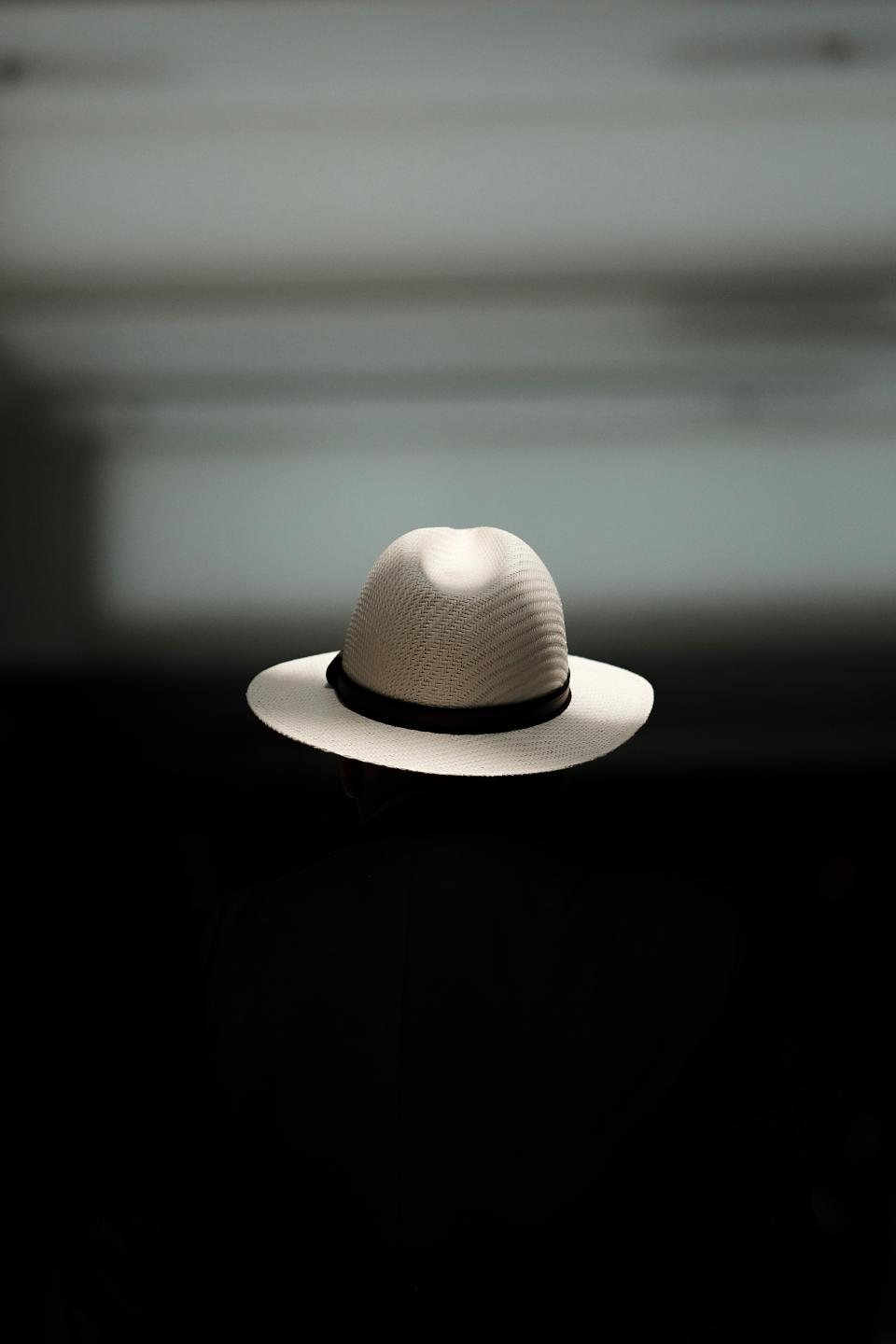 White woven straw hat with a black band, lit against a dark background
