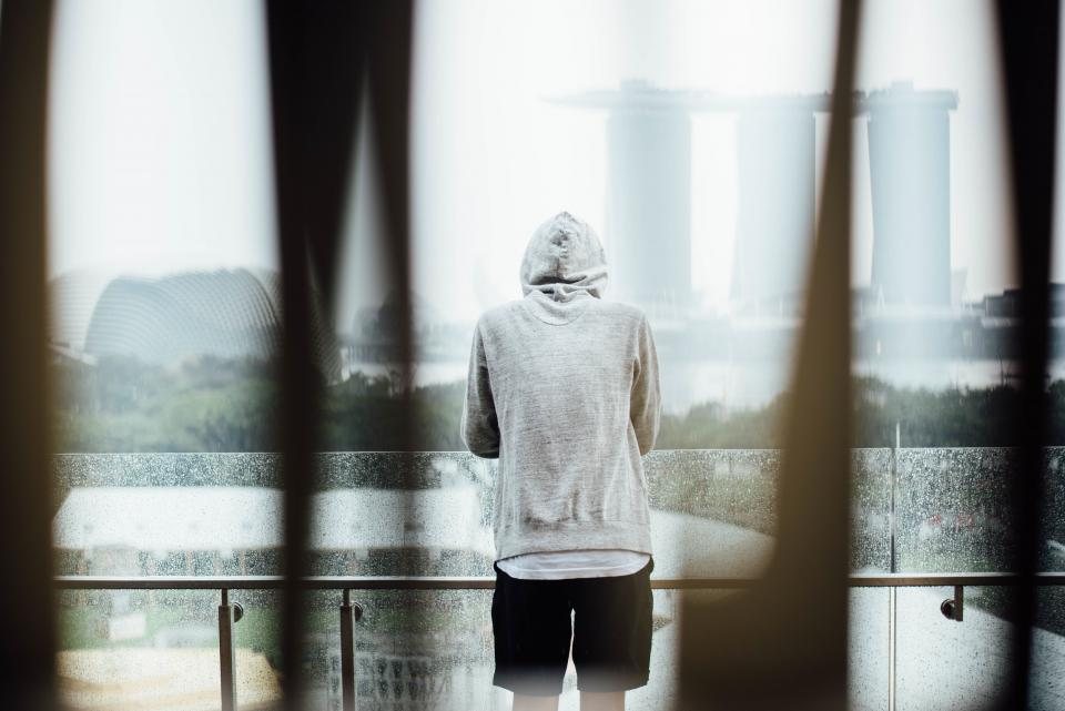 Person in a grey hoodie seen from behind, looking out over a misty city skyline