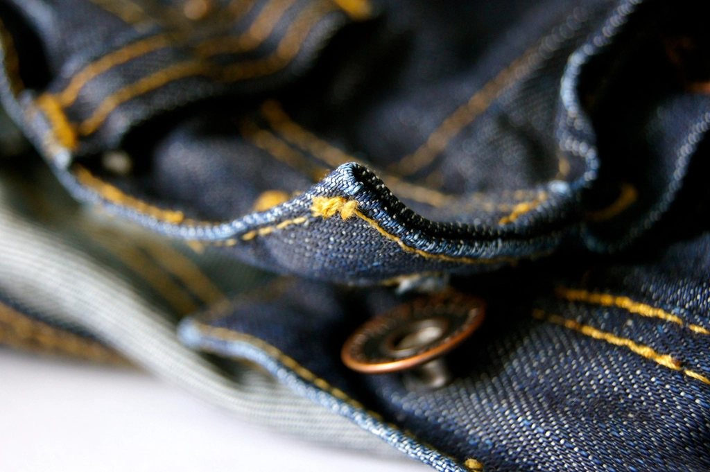 Close-up of raw indigo denim with a copper button and gold stitching