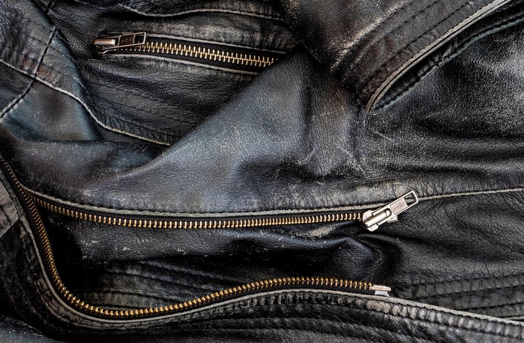 Close-up of a worn black leather jacket with brass zips