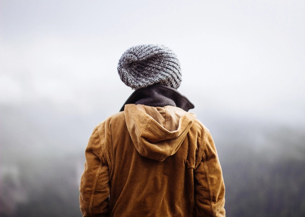 Model in a grey beanie and mustard cord jacket against fog