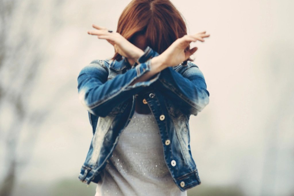 Woman in a denim jacket crossing her arms in front of her face