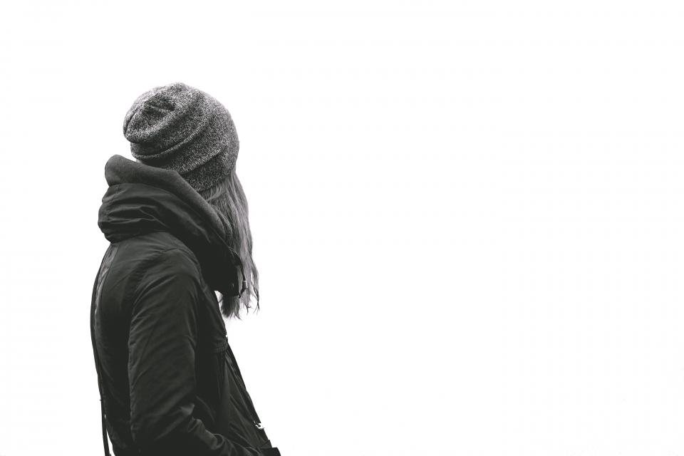 Monochrome profile of a person in a black parka and grey beanie, facing away, on white
