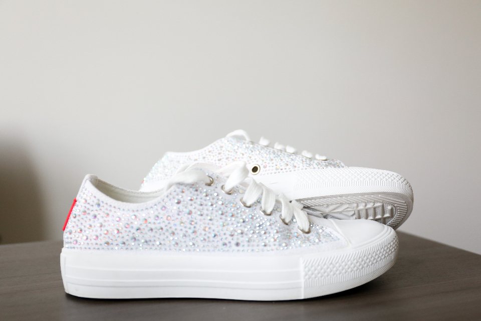 Pair of white canvas low-top sneakers with a crystal-embellished upper on a dark table
