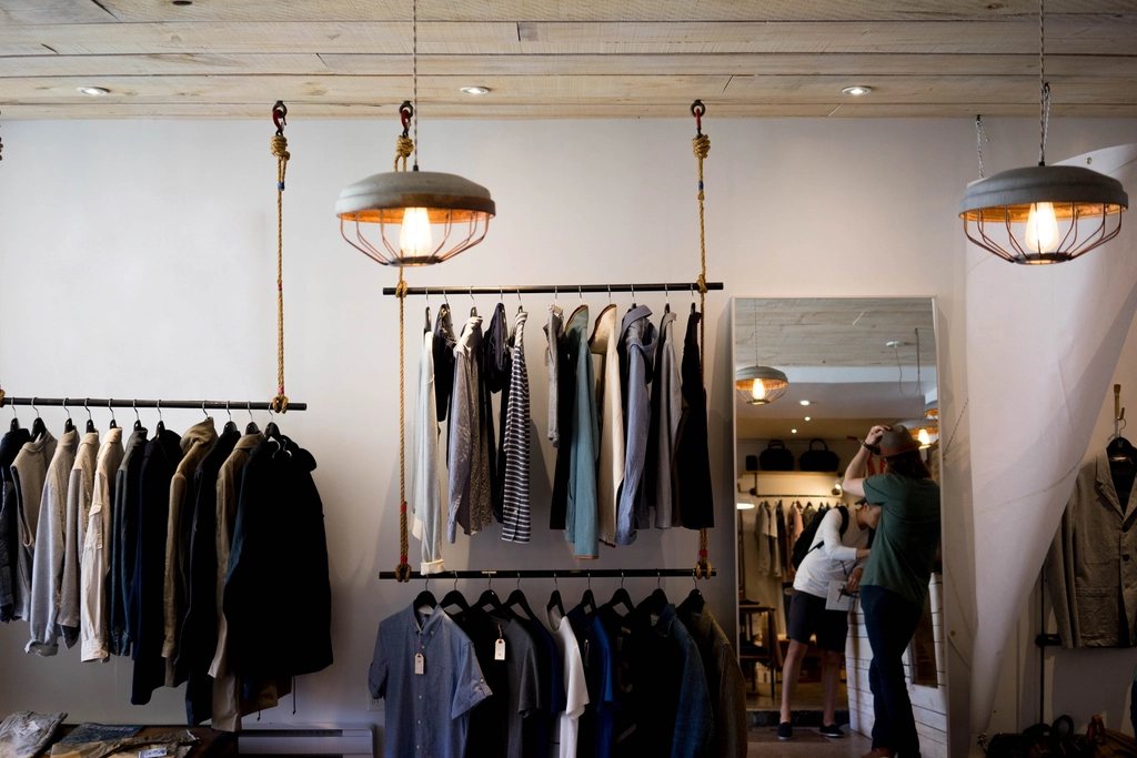 Boutique interior with clothing on rope-hung rails, pendant lamps and a mirror