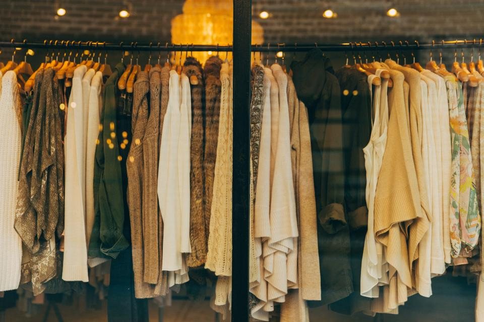 Rail of knitwear and neutral tops seen through a shop window under warm lights
