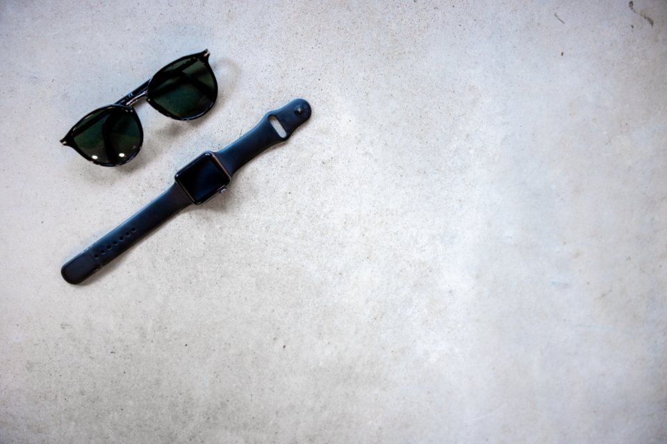 Black sunglasses and a smartwatch with a black strap on concrete