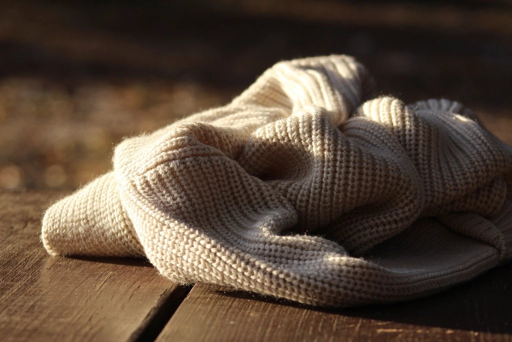 Cream knit sweater lying on a wooden deck in warm low sunlight