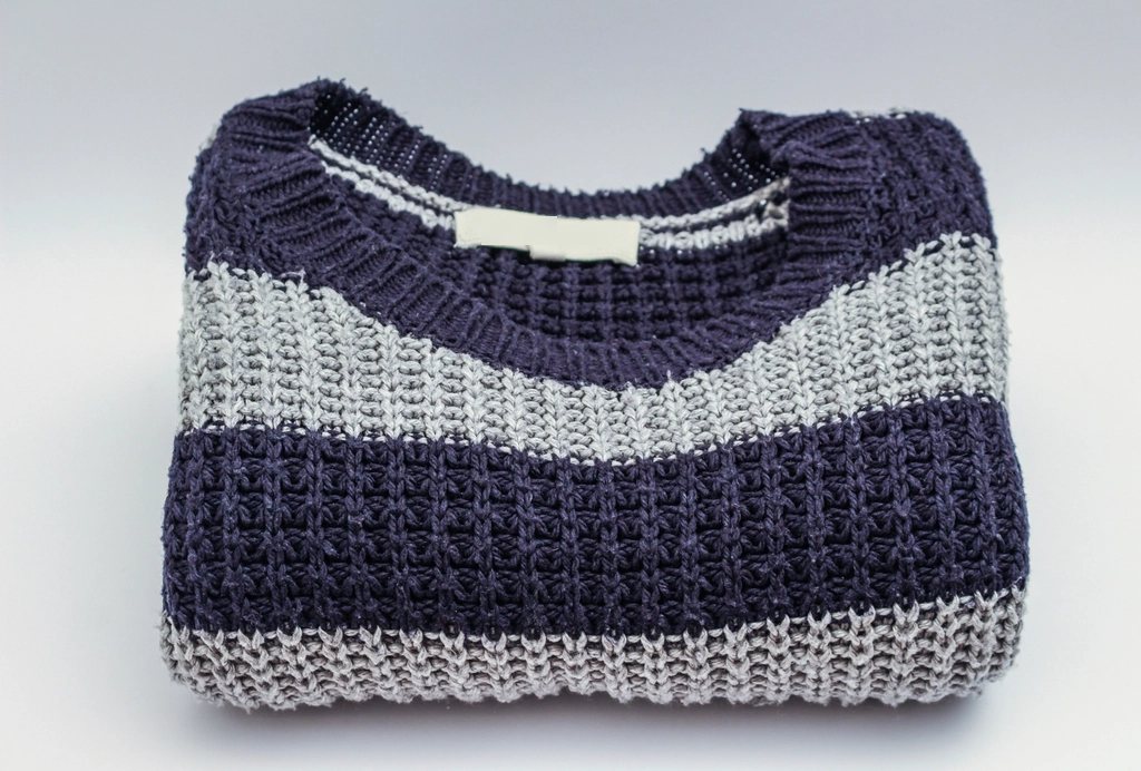 Folded navy and grey striped chunky-knit sweater on a pale grey background