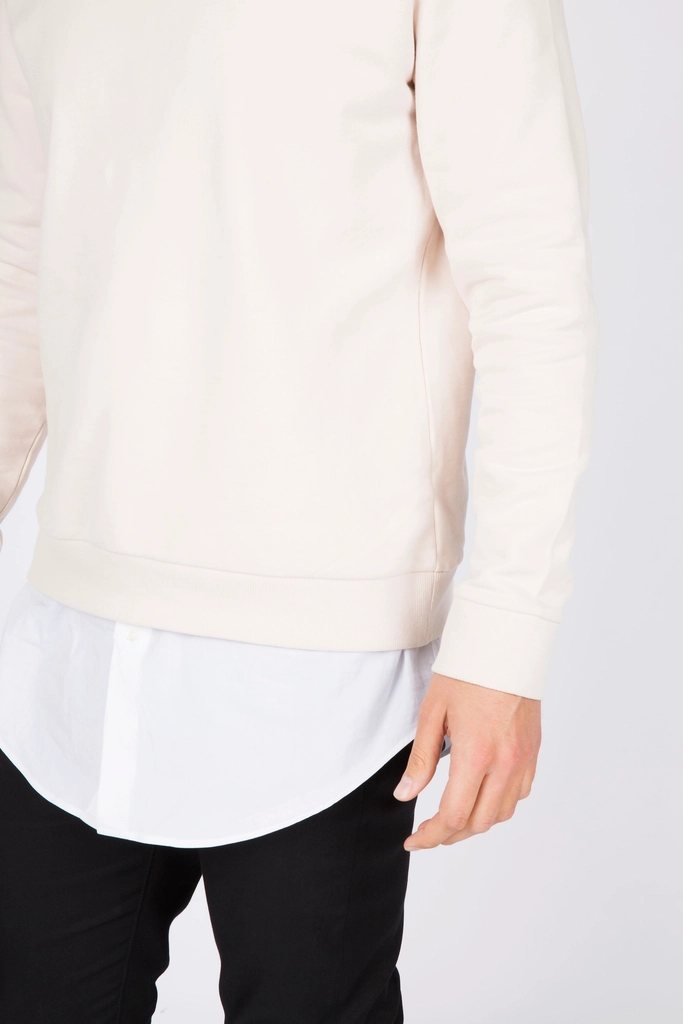 Cropped studio shot of a cream crew-neck sweatshirt layered over a white shirt with black trousers