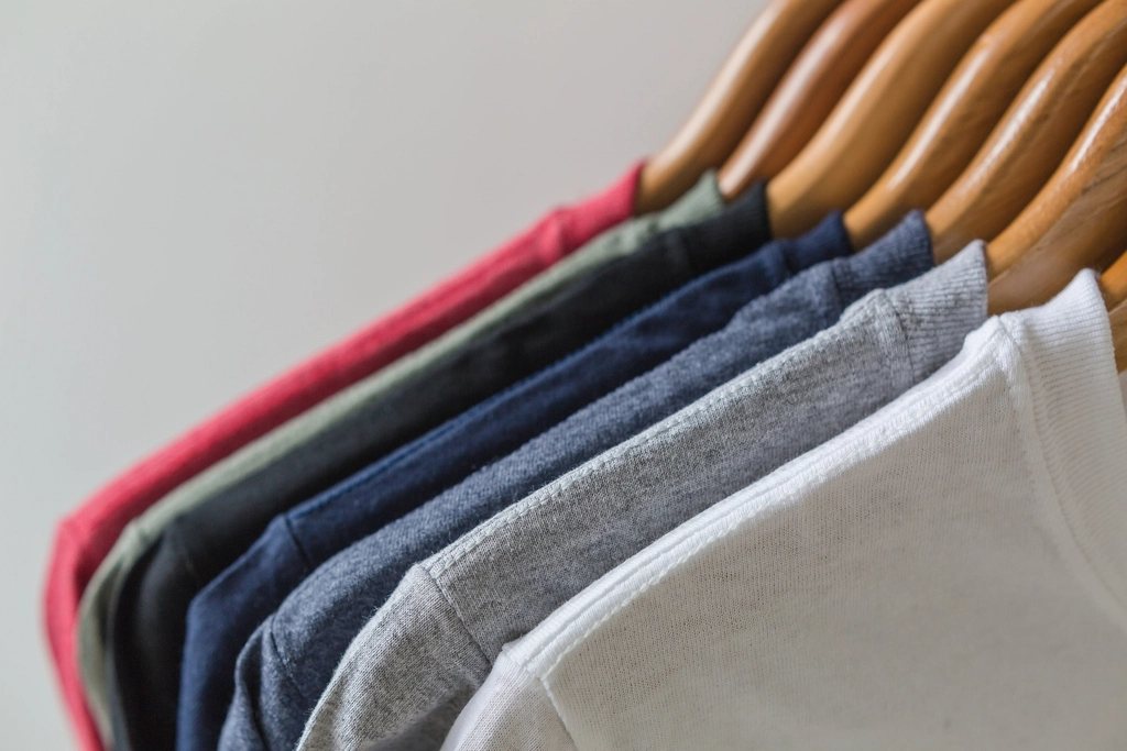 Close-up of tee shoulders in red, olive, black, navy, grey and white on wooden hangers