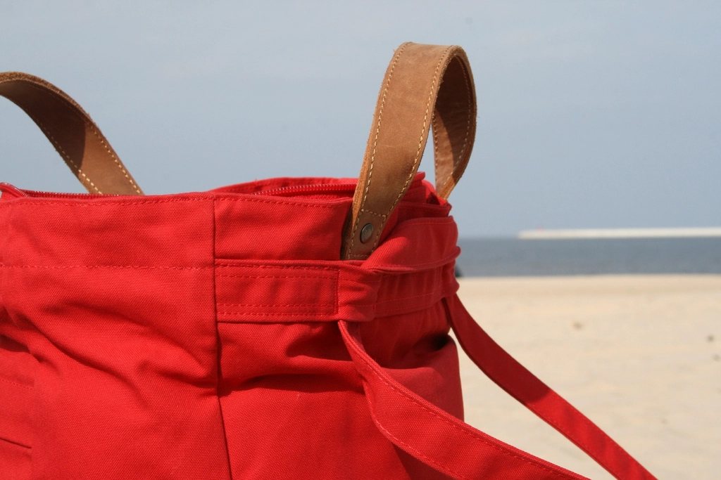 Close-up of a red canvas tote with tan leather handles on a beach