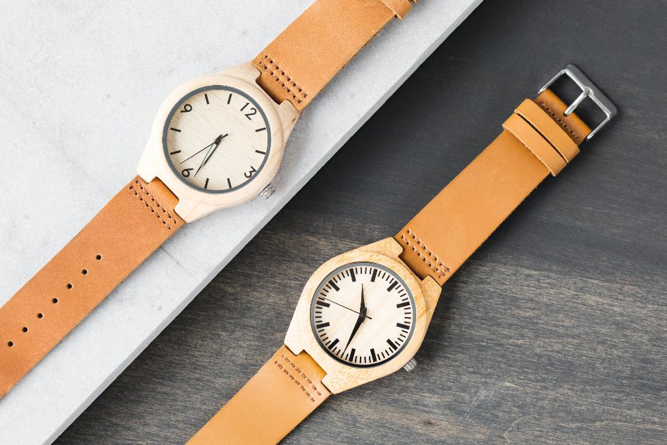 Two wooden watches with tan leather straps on grey stone and slate